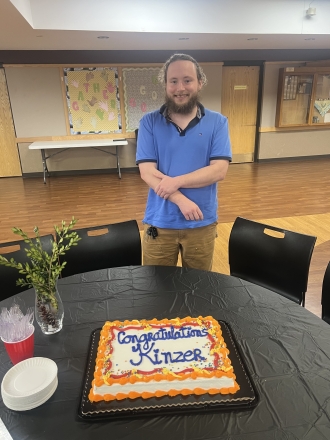 A man named Kinzer who graduated the Hillcrest Platte County HPC Transitional Housing Program Standing by his graduation cake smiling
