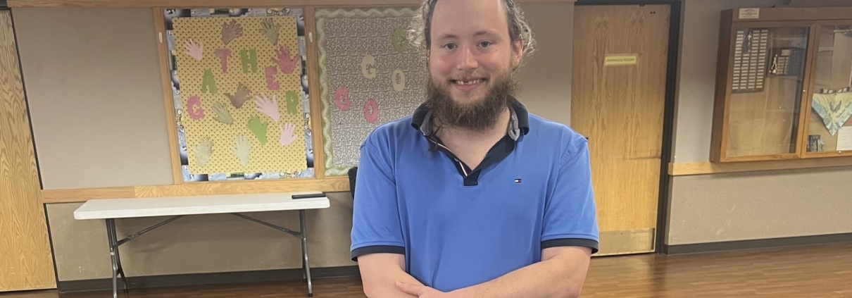 A man named Kinzer who graduated the Hillcrest Platte County HPC Transitional Housing Program Standing by his graduation cake smiling